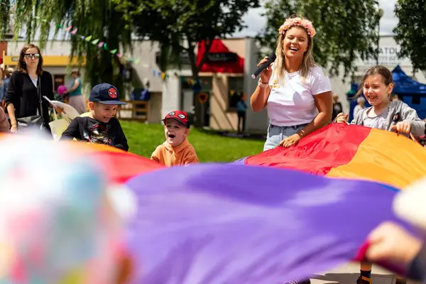 Animatorka z mikrofonem i roześmiane dzieci podczas zabawy z chustą animacyjną na festynie